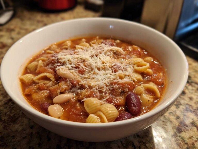 A close-up of a white bowl filled with hot pasta e fagioli soup, topped with grated Parmesan cheese.