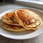 A stack of three golden brown, fluffy buttermilk pancakes served on a white plate.