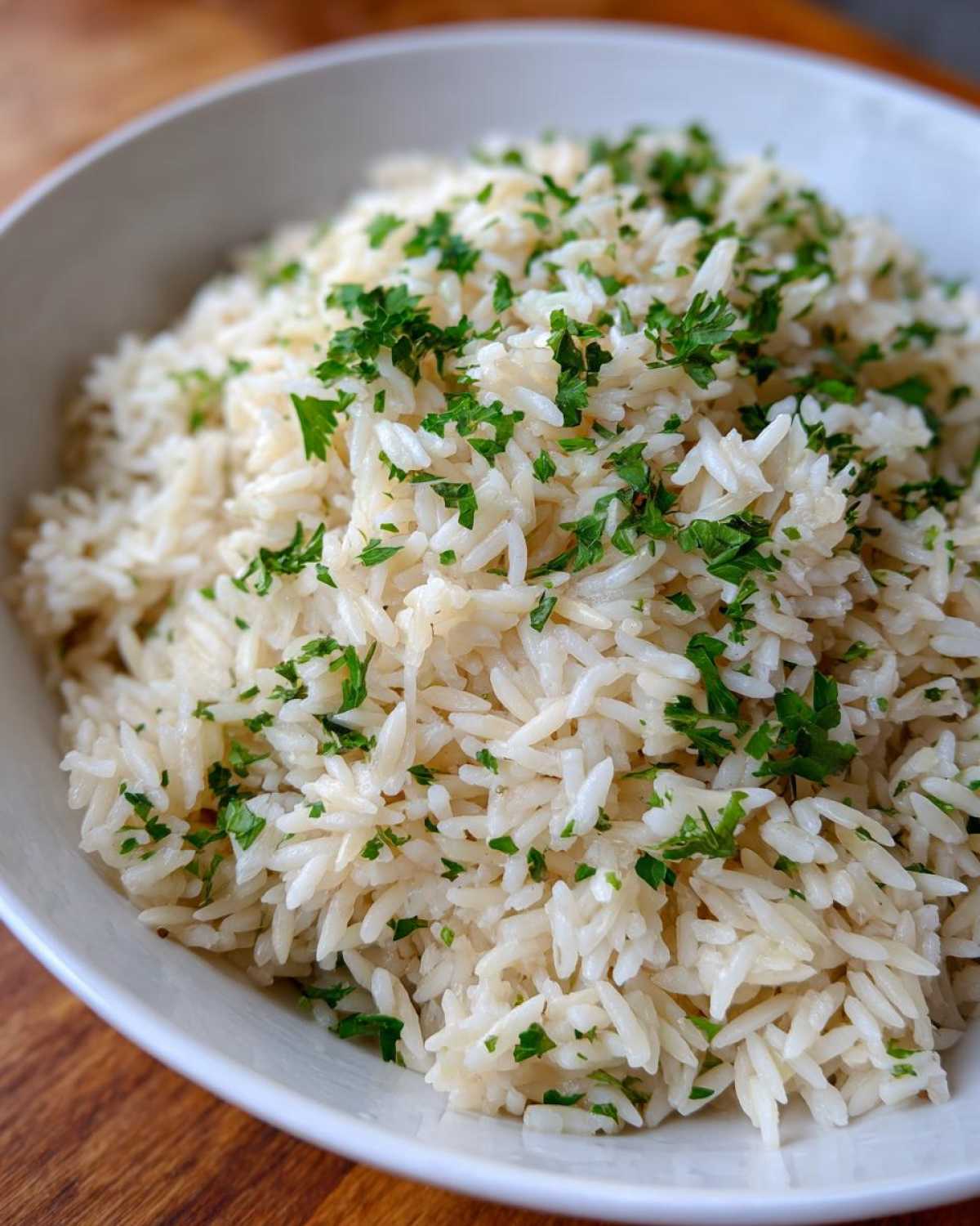 Close-up of fluffy white rice pilaf served in a white bowl and garnished generously with chopped fresh parsley.