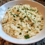Close-up of fluffy rice pilaf served in a white bowl and garnished generously with chopped fresh parsley.