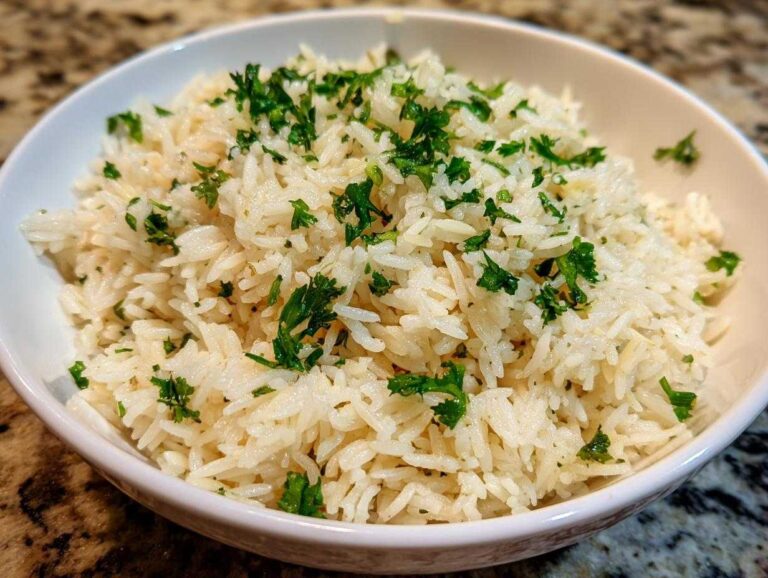 A close-up of fluffy white rice pilaf served in a white bowl and garnished generously with chopped green parsley.