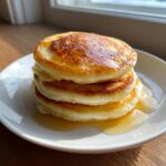 A tall stack of three fluffy sourdough discard pancakes drizzled generously with golden syrup on a white plate.