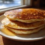 A stack of three fluffy sourdough discard pancakes drizzled generously with golden syrup.