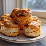 A stack of fluffy sweet potato biscuits topped generously with a thick, creamy caramel or dulce de leche topping.