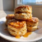 A stack of four fluffy sweet potato biscuits drizzled generously with a shiny, amber glaze.