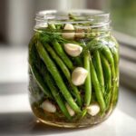 Close-up of fresh green beans being pickled in a jar with dill, garlic cloves, and peppercorns to make dilly beans.