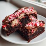 Close-up of fudgy candy cane brownies with a white cream cheese swirl and crushed peppermint topping on a white plate.
