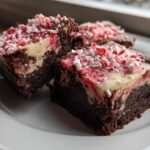 Three squares of fudgy candy cane brownies with a cream cheese swirl and crushed peppermint topping on a white plate.