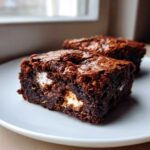 Close-up of two fudgy hot chocolate brownies with visible melted marshmallow pieces on a light plate.