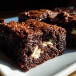 A close-up of a fudgy, dark chocolate hot chocolate brownie square with visible white chocolate chunks.