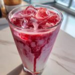 Close-up of a tall glass filled with iced strawberry milk, showing swirls of pink and red syrup.