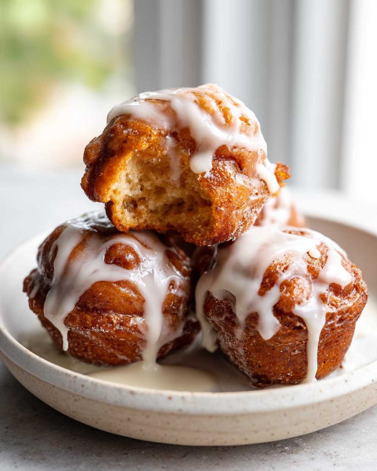 A stack of three glazed baked apple fritter treats, with one having a bite taken out to show the soft interior.