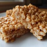 Close-up of two gooey peanut butter rice krispie treats squares stacked slightly on a white plate.