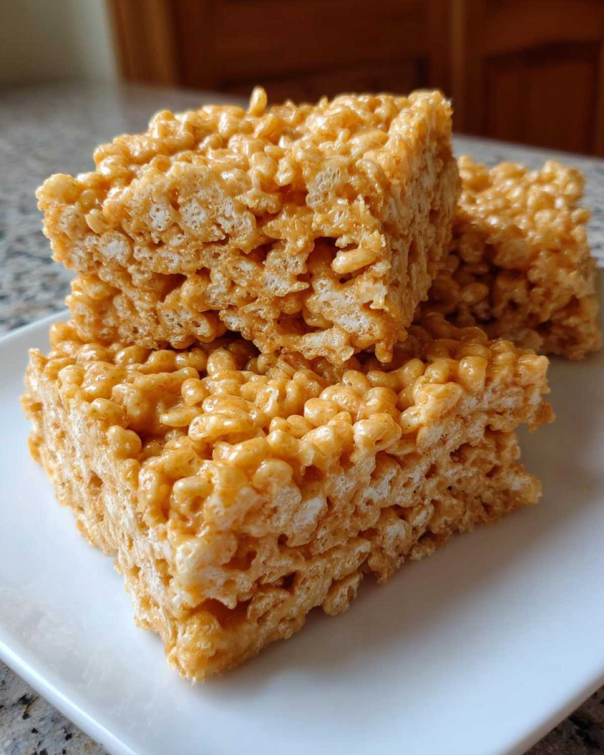 Close-up of three gooey peanut butter rice krispie treats stacked on a white plate.