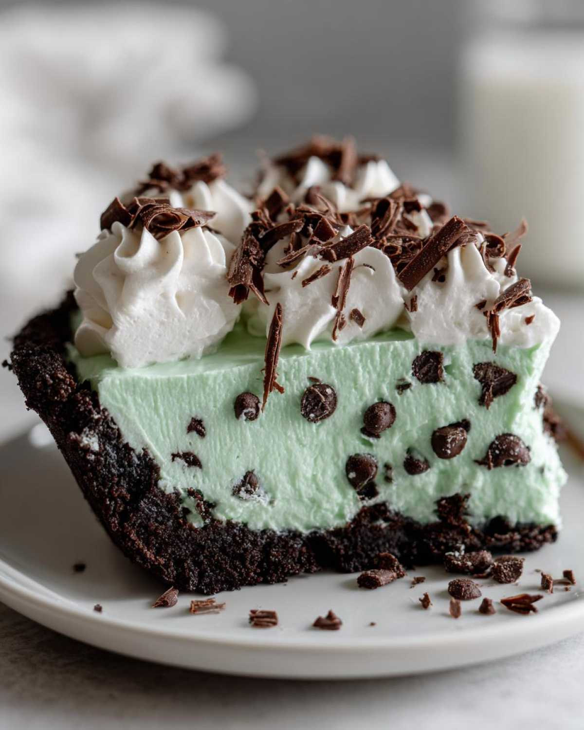 Close-up of a slice of grasshopper pie showing mint filling with chocolate chips, topped with whipped cream and chocolate shavings.