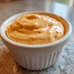 Close-up of creamy, orange-hued homemade big mac sauce served in a small white fluted ramekin.
