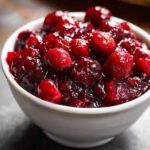 Close-up of rich, homemade cranberry sauce with whole berries in a small white bowl.