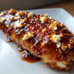 A close-up of a juicy chicken breast covered in a thick, glossy hot honey glaze and topped with crumbles of feta cheese.