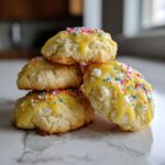 A stack of four soft Italian ricotta cookies topped with bright yellow glaze and rainbow sprinkles.