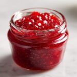 Close-up of a small glass jar filled with vibrant, chunky strawberry freezer jam.