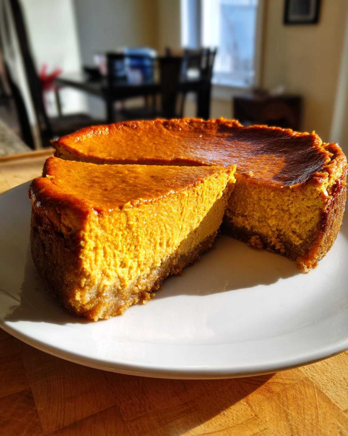 A rich, orange keto pumpkin cheesecake with a slice cut out, sitting on a white plate.