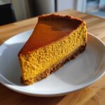A perfect slice of rich, orange keto pumpkin cheesecake with a dark crust on a white plate.