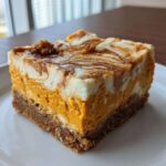 A close-up of a single, perfectly cut square of pumpkin cheesecake bars with a marbled top.