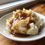 A serving of fluffy mashed potatoes generously covered with smooth, rich chicken gravy in a white bowl.
