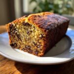 A close-up of a moist slice of chocolate chip banana bread recipe on a white plate.