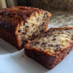 Close-up of a moist chocolate chip banana bread recipe loaf, with one slice cut and resting beside it.