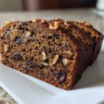 Three moist slices of date nut bread, studded with dates and walnuts, served on a white rectangular plate.