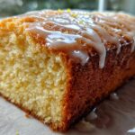 Close-up of a moist lemon loaf cake slice showing the crumb and thick, dripping lemon glaze.