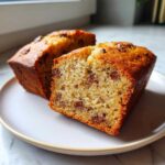 Close-up of two halves of a moist mini banana bread loaf filled with chocolate chips on a white plate.
