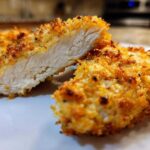 Close-up of parmesan crusted chicken cut in half showing juicy interior and crispy golden coating.