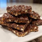A stack of rich, dark chocolate peanut butter pretzel bark pieces piled high on a white rectangular plate.