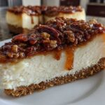 A close-up slice of pecan pie cheesecake featuring a thick graham cracker crust and gooey pecan topping.