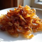Close-up of a mound of deeply golden brown caramelized onions glistening on a white plate.