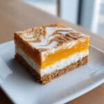 A single serving of layered pumpkin cheesecake bars with a graham cracker crust and marbled top.