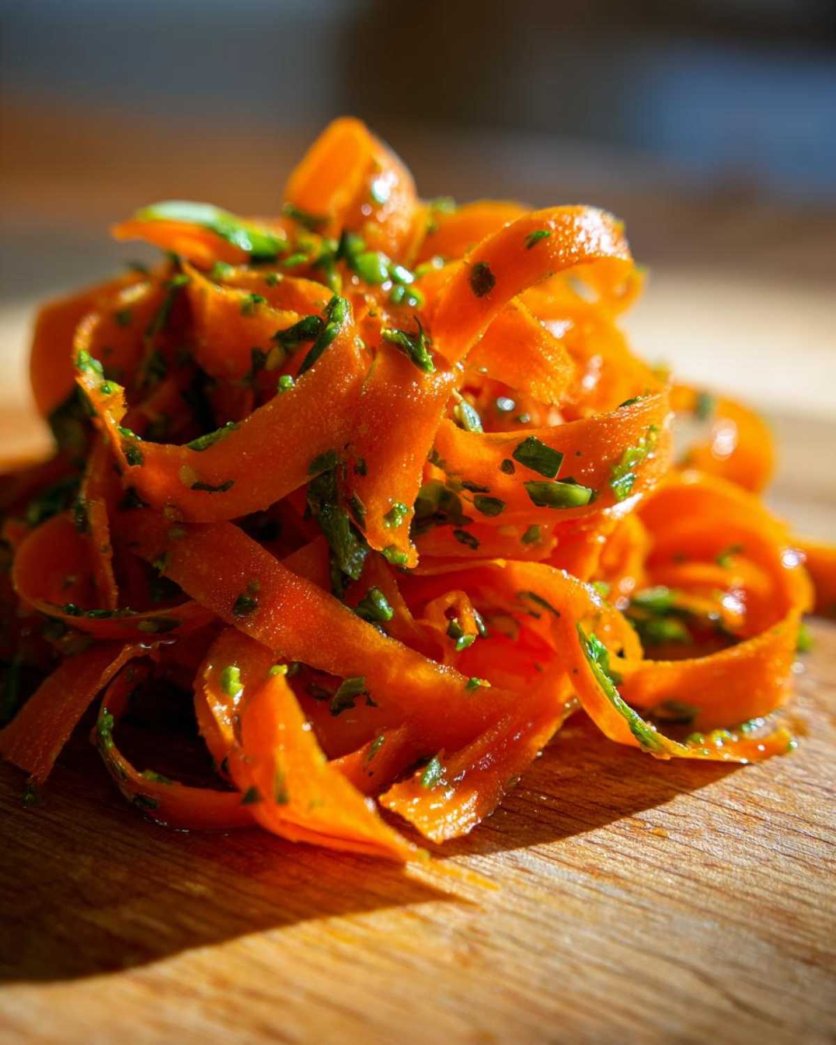 Close-up of bright orange, shaved ribbons in a raw carrot salad, tossed with green herbs.