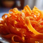 Close-up of bright orange, thinly shaved ribbons of carrot ready for a raw carrot salad, glistening slightly.