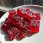 Close-up of vibrant red, sugar-coated cubes resembling cinnamon rock candy piled on a white plate.