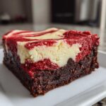 A rich, square slice of red velvet cheesecake brownies showing a dark brownie base and a marbled red and cream cheese topping.