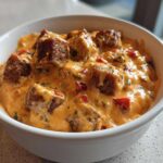 A close-up view of the rich, creamy sausage cheese dip loaded with chunks of browned sausage and red peppers in a white serving bowl.