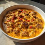 Close-up of a rich, creamy sausage cheese dip topped with red peppers and herbs in a white bowl.