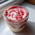 Close-up of a single-serving Protein Cheesecake in a glass jar with a vibrant red berry swirl topping.