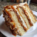Close-up of a decadent slice of caramel crunch cake showing multiple layers of sponge, cream, and caramel drizzle.