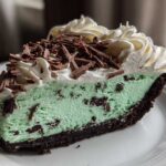 A rich slice of grasshopper pie with a mint green filling, chocolate crust, whipped cream, and chocolate shavings.