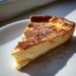 A perfect slice of creamy egg custard dessert dusted with cinnamon on a white plate.