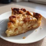 A close-up of a generous slice of moist swedish apple cake, featuring caramelized edges, served on a white plate.