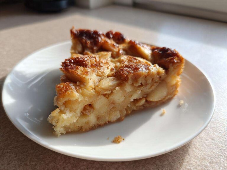 A close-up of a generous slice of moist swedish apple cake, featuring caramelized edges, served on a white plate.